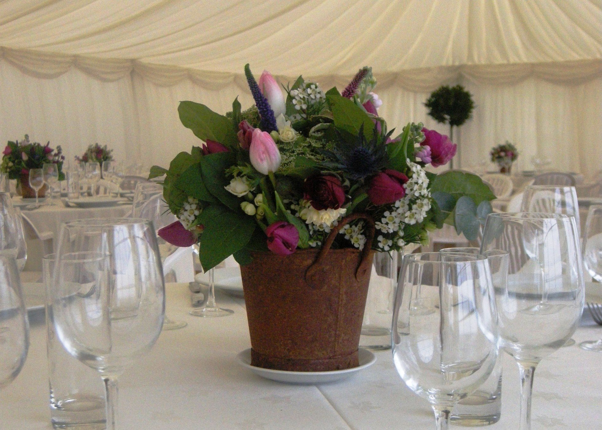 Photo of wedding table centre with flowers in rusty pot and glassware