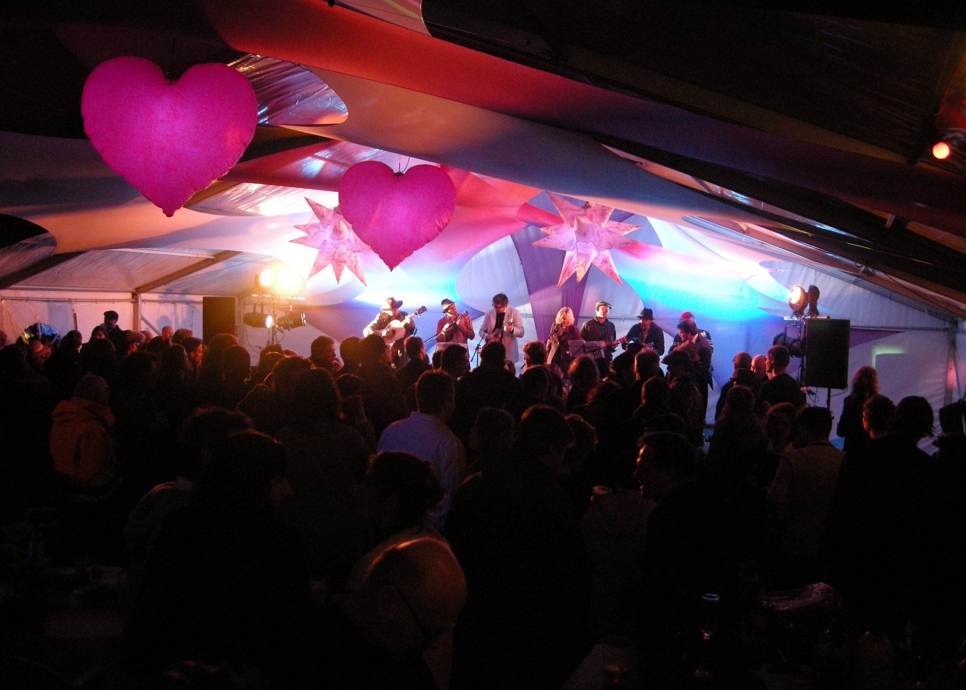 Inside of marquee at night with crowd watching Ukelele band on stage, inflatables & stretch lycra decor
